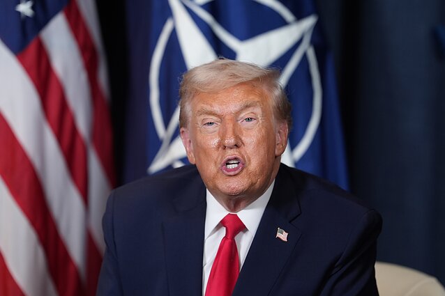 Donaldas Trumpas priešais NATO ir JAV vėliavas Donaldas Trumpas priešais NATO ir JAV vėliavas